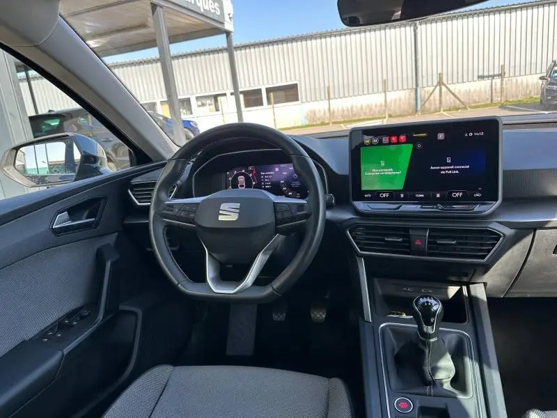 Vue intérieure frontale du poste de conduite du SEAT LEON ST 2025 avec volant multifonction, écran tactile et levier de vitesse manuel.