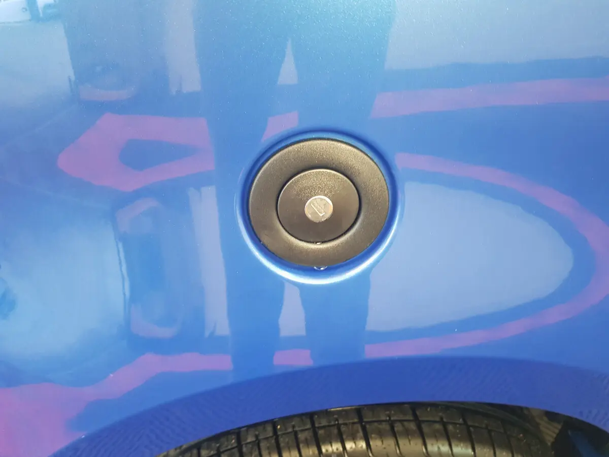 Gros plan sur la trappe de réservoir bleu d'une Aixam Ambition 0.5 City Sport, avec pneu partiellement visible en bas.