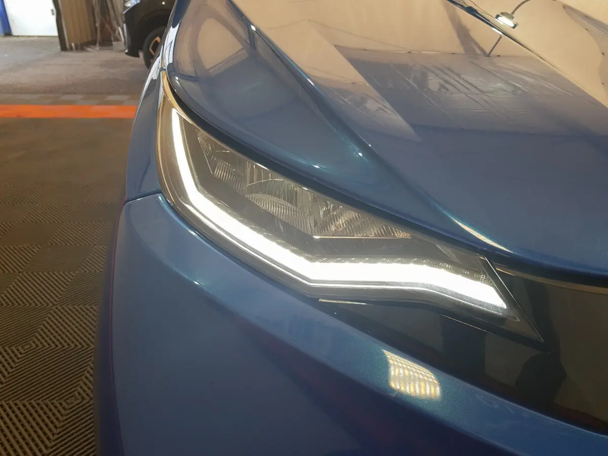 Gros plan sur le phare avant gauche allumé de l'AIXAM AMBITION 0.5 CITY SPORT bleu 2026 avec carrosserie brillante.