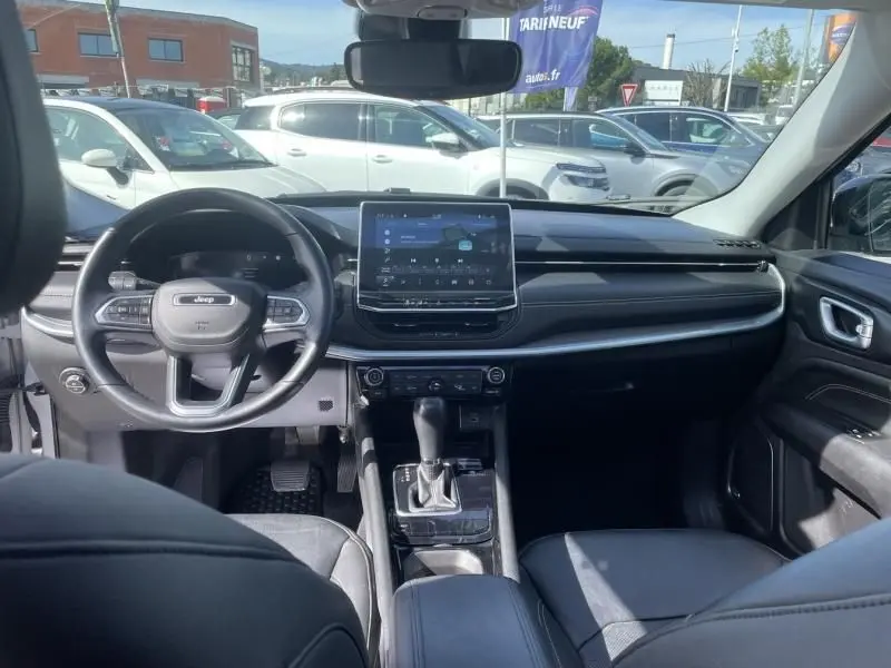 Vue intérieure avant du Jeep Compass 2023 gris métal, mettant en valeur le tableau de bord moderne et l'écran tactile central.