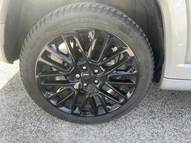 Gros plan sur la roue avant droite d’un Jeep Compass gris métal 2023 avec jante noire brillante à multiples branches.
