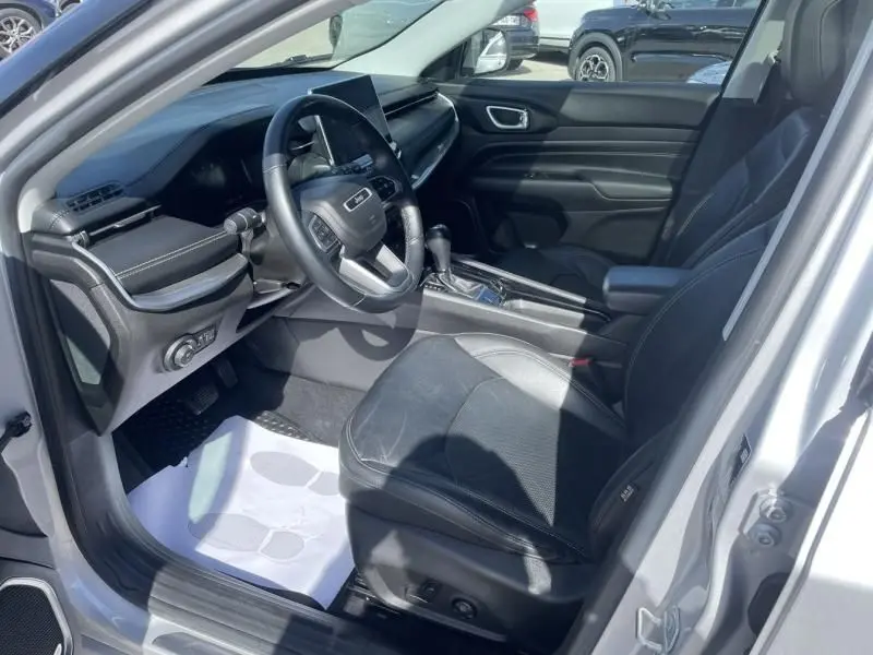 Vue intérieure côté conducteur du Jeep Compass gris métal 2023, montrant le volant, la console centrale et les sièges en cuir noir.