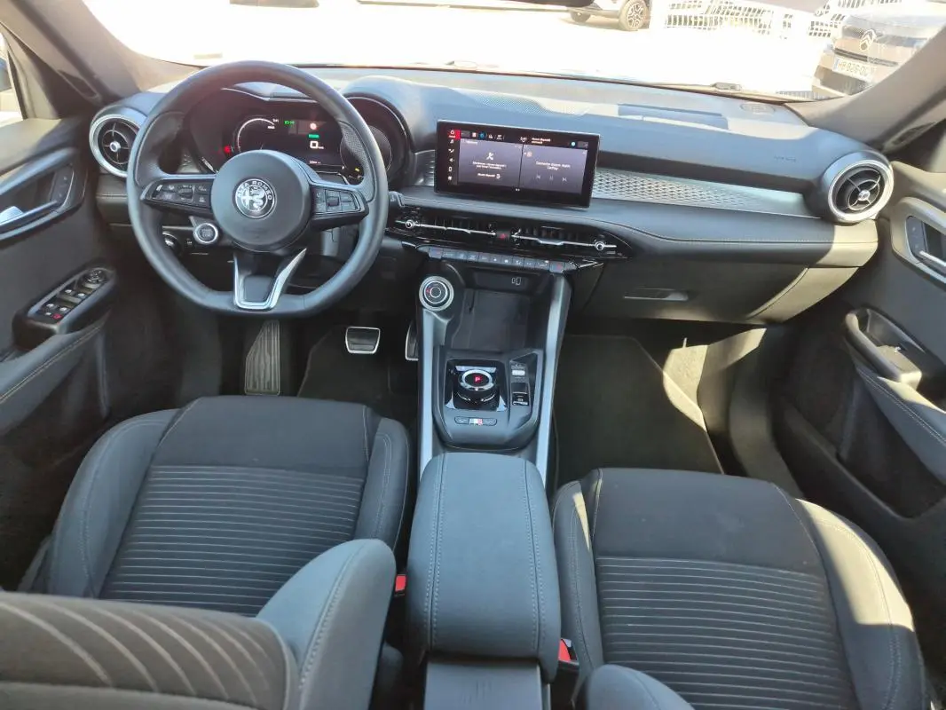 Vue intérieure frontale de l'Alfa Romeo Tonale 2025, tableau de bord moderne avec écran tactile et volant sport noir.