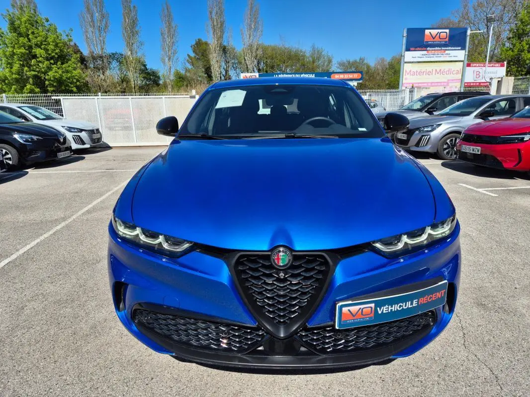 Vue avant d'une Alfa Romeo Tonale bleu vif avec calandre distinctive et feux LED allumés, en extérieur sur parking.