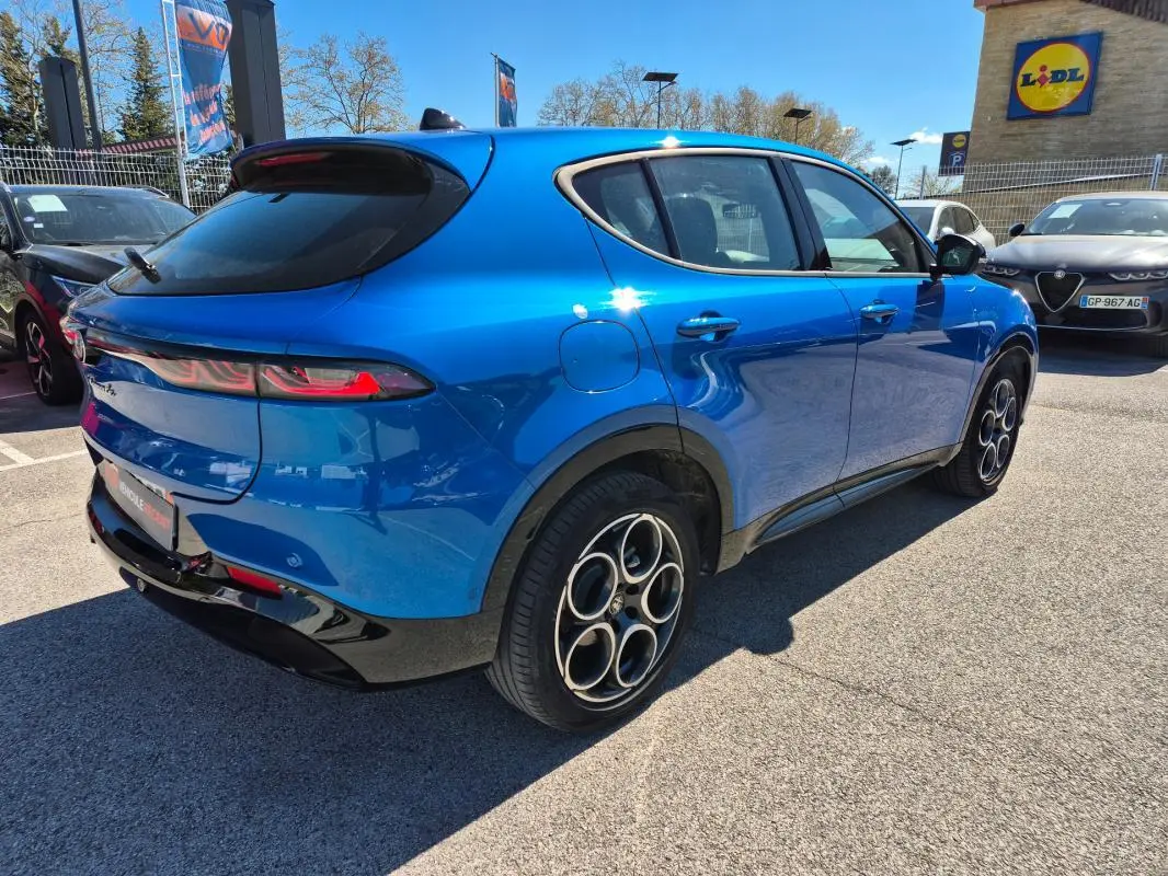Vue 3/4 arrière droite d'une Alfa Romeo Tonale bleu avec jantes alliage 18 pouces et feux arrière allumés.