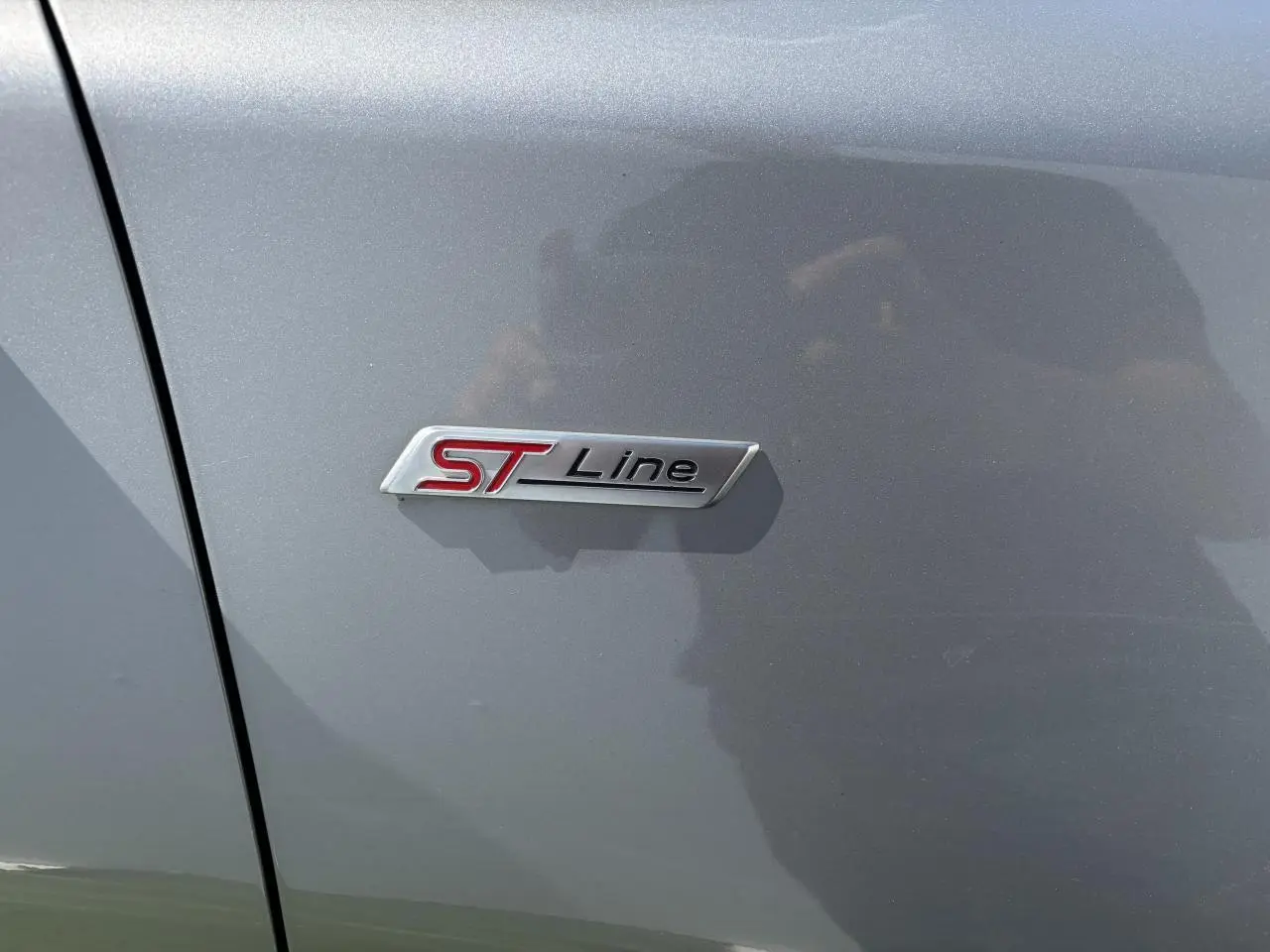 Gros plan sur le badge ST-Line rouge et argent sur la porte côté gauche d’un Ford Puma gris métal.