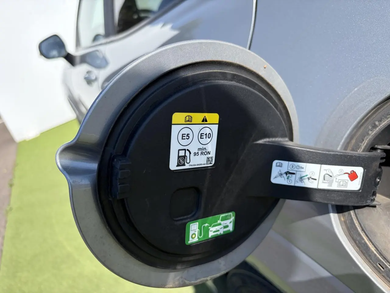 Gros plan sur la trappe à carburant ouverte d’un Ford Puma gris métal, avec consignes de carburant visibles.