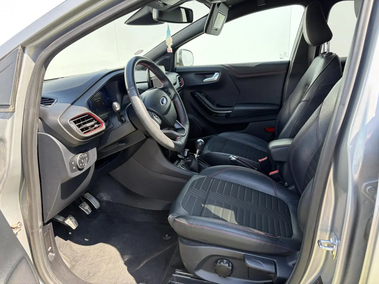 Vue intérieure côté conducteur du Ford Puma gris métal 2020, sièges noirs avec surpiqûres rouges et volant ST-Line.