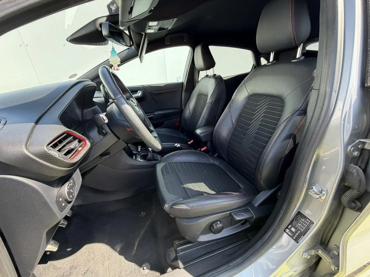 Vue intérieure côté conducteur du Ford Puma gris métal 2020, sièges noirs avec surpiqûres rouges et volant ST-Line.