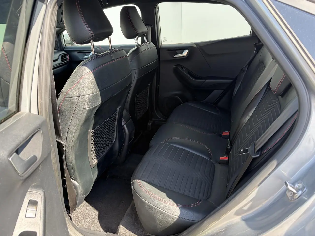 Vue côté gauche de l’intérieur arrière du Ford Puma gris métal, avec sièges noirs et surpiqûres rouges visibles.