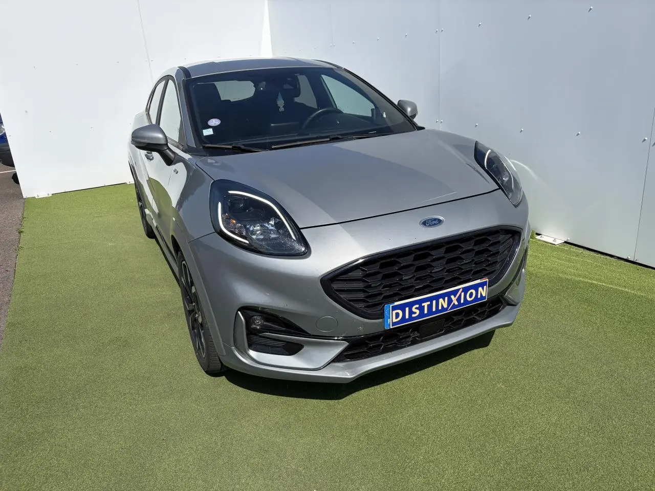Vue 3/4 avant d'un Ford Puma gris métal avec calandre noire et jantes alliage noires sur sol vert.