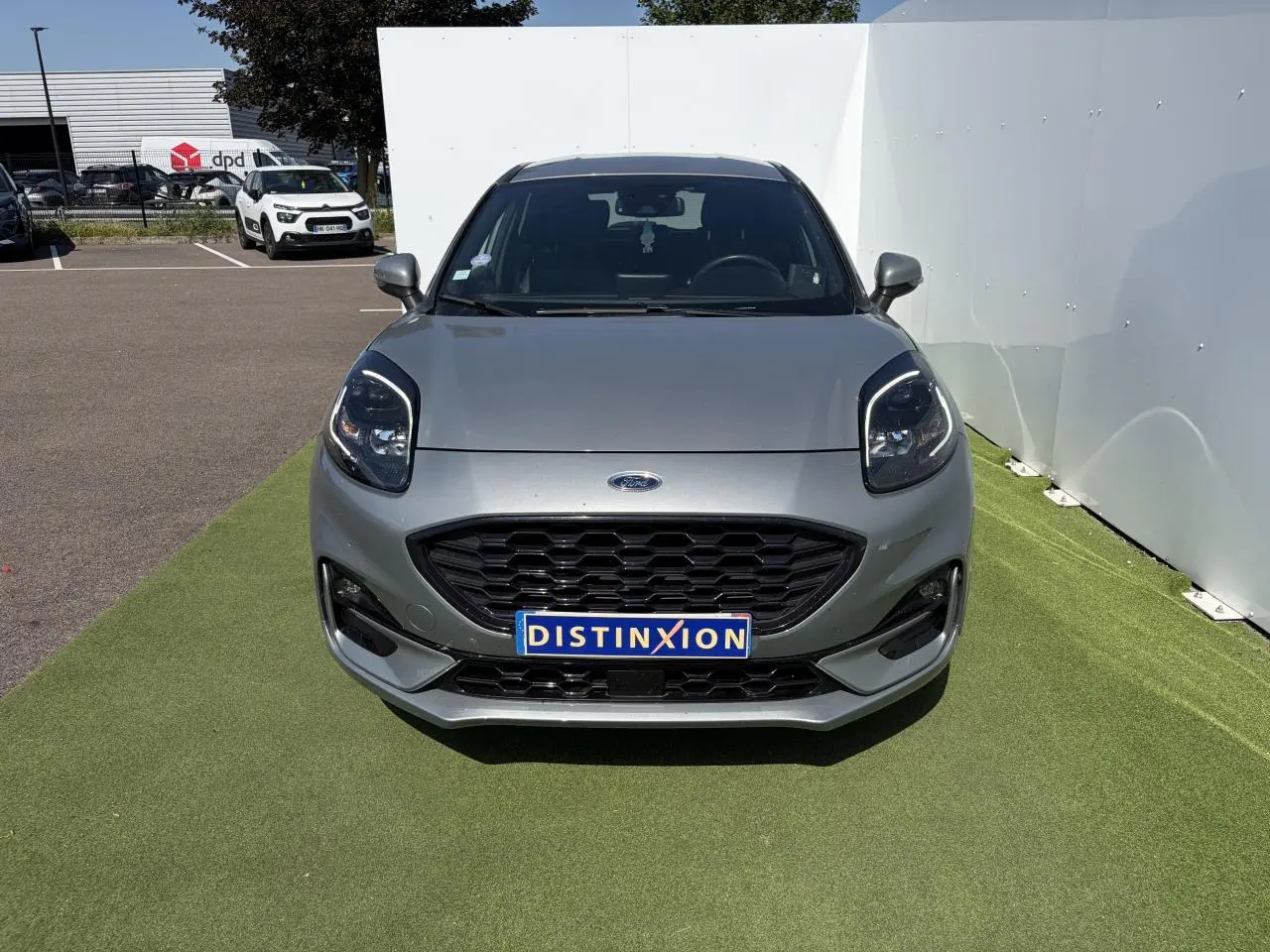 Vue avant d'un Ford Puma gris métal avec calandre noire et phares LED, sur fond d'herbe synthétique.