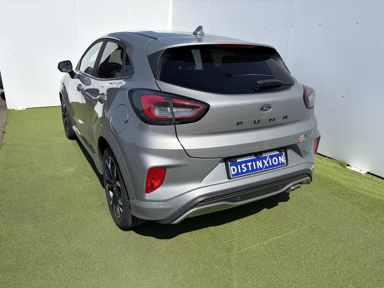 Vue 3/4 arrière droite d'un Ford Puma gris métal avec badges ST-Line et jantes alliage noires sur fond vert.