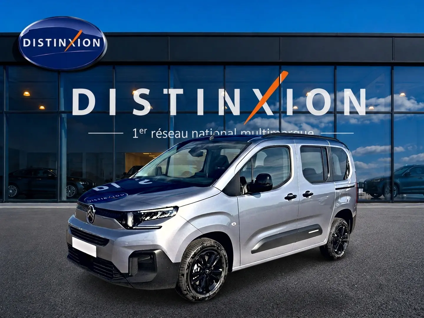 Vue 3/4 avant droit d'un Citroën Berlingo gris acier avec jantes noires devant une vitrine Distinxion.