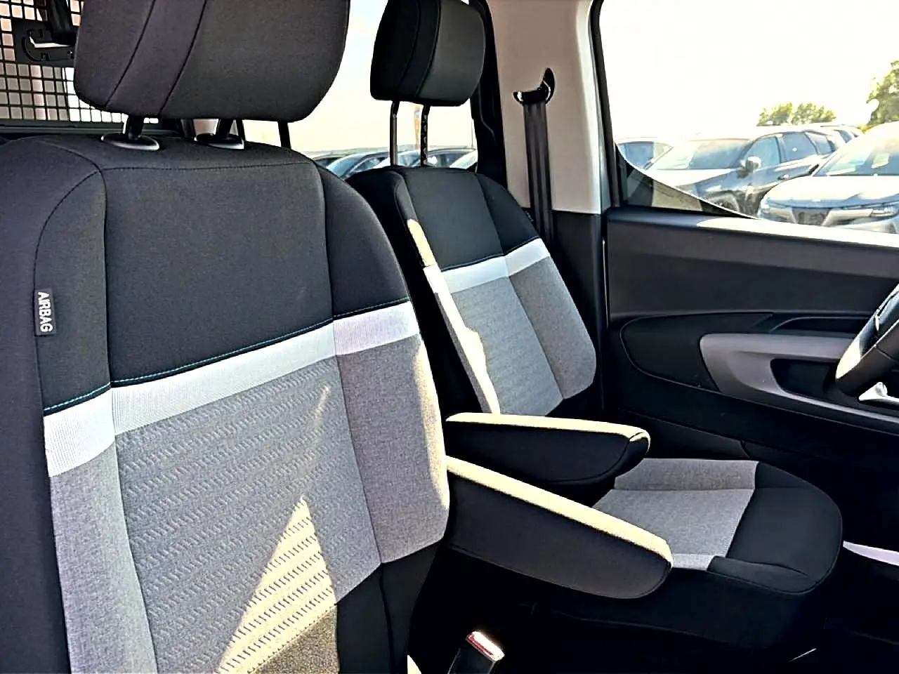 Vue rapprochée des sièges avant gris clair et noir du Citroën Berlingo N1 2026 avec accoudoirs centraux déployés.