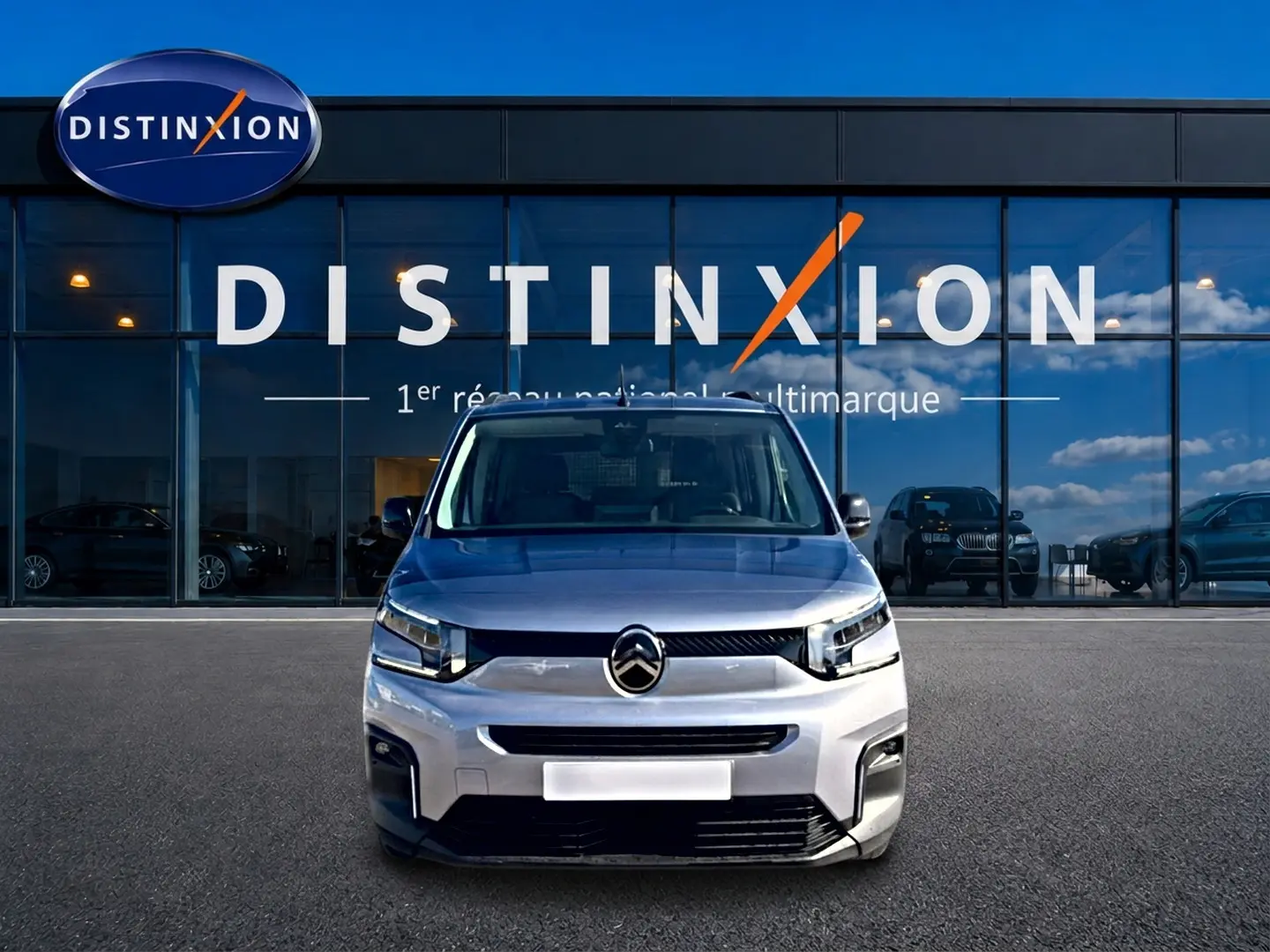 Vue frontale d'un Citroën Berlingo 2026 gris acier, avec calandre distinctive et logo centré devant un showroom Distinxion.