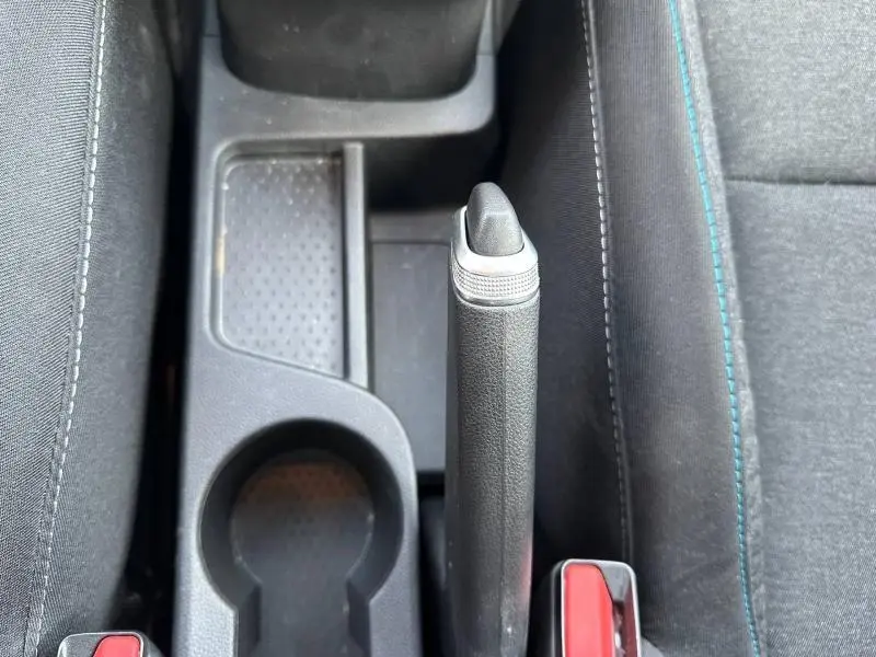Vue plongeante sur le frein à main manuel noir et les sièges tissu gris avec surpiqûres bleues du Renault Captur 2025.