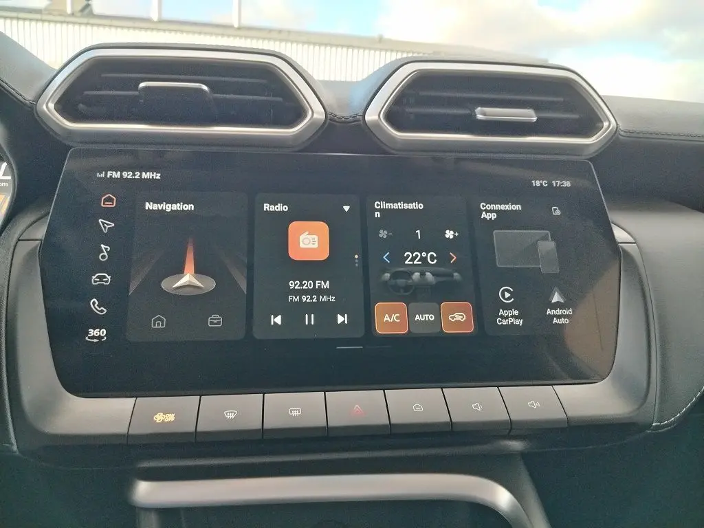 Écran tactile central du MG MOTOR ZS 1.5 l Hybrid 2026, affichant navigation, radio et climatisation, intérieur noir.