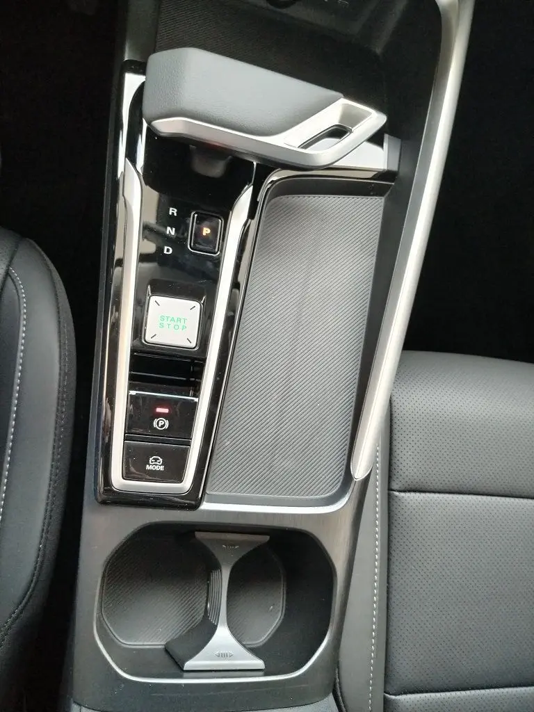 Vue plongeante sur la console centrale noire du MG MOTOR ZS 1.5 l Hybrid 197 LUXURY avec levier de vitesses et bouton start/stop.