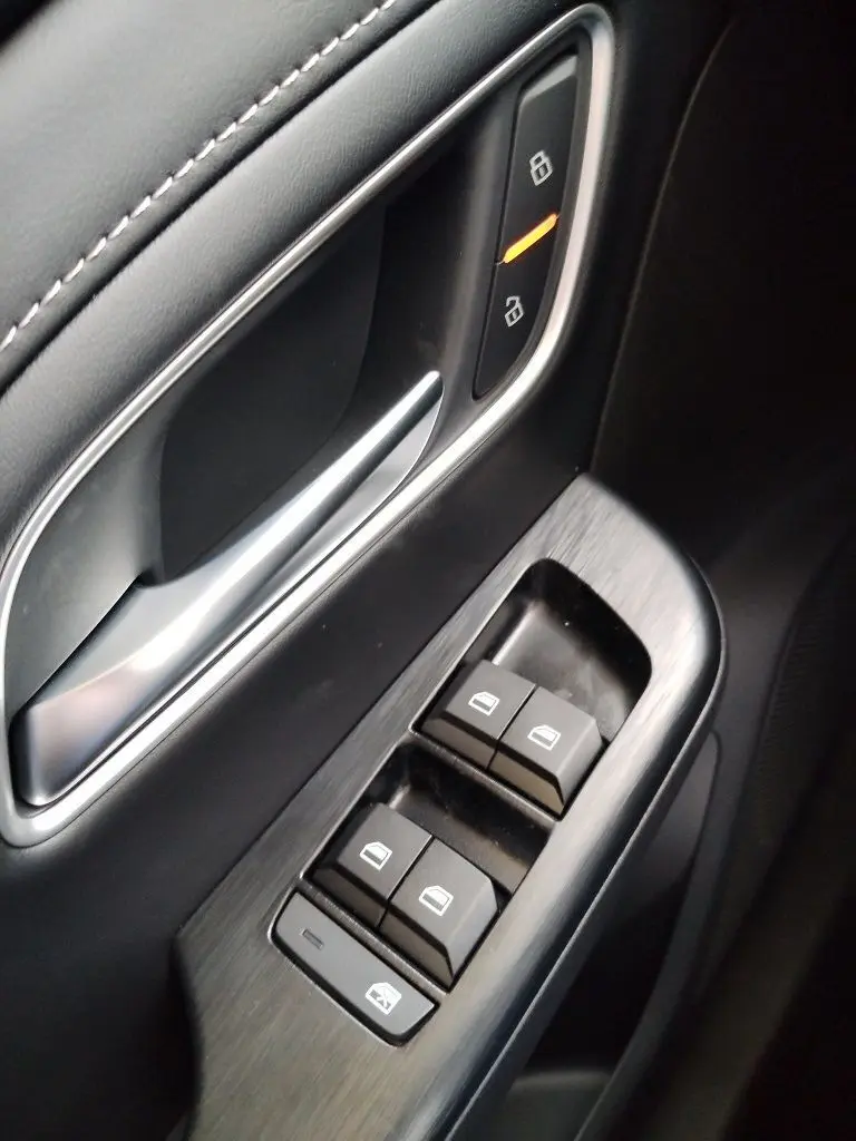 Gros plan sur la commande des vitres et la poignée intérieure côté gauche du MG ZS 1.5 l Hybrid+ 197 Luxury en finition noire.