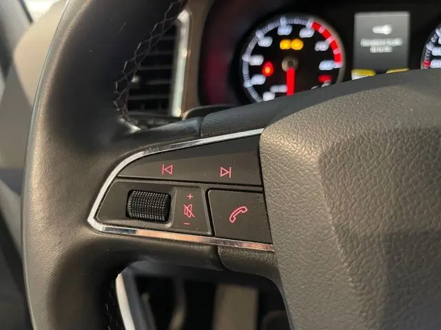 Gros plan sur les commandes audio et téléphone au volant d’un SEAT Ateca blanc Nevada, tableau de bord en arrière-plan.