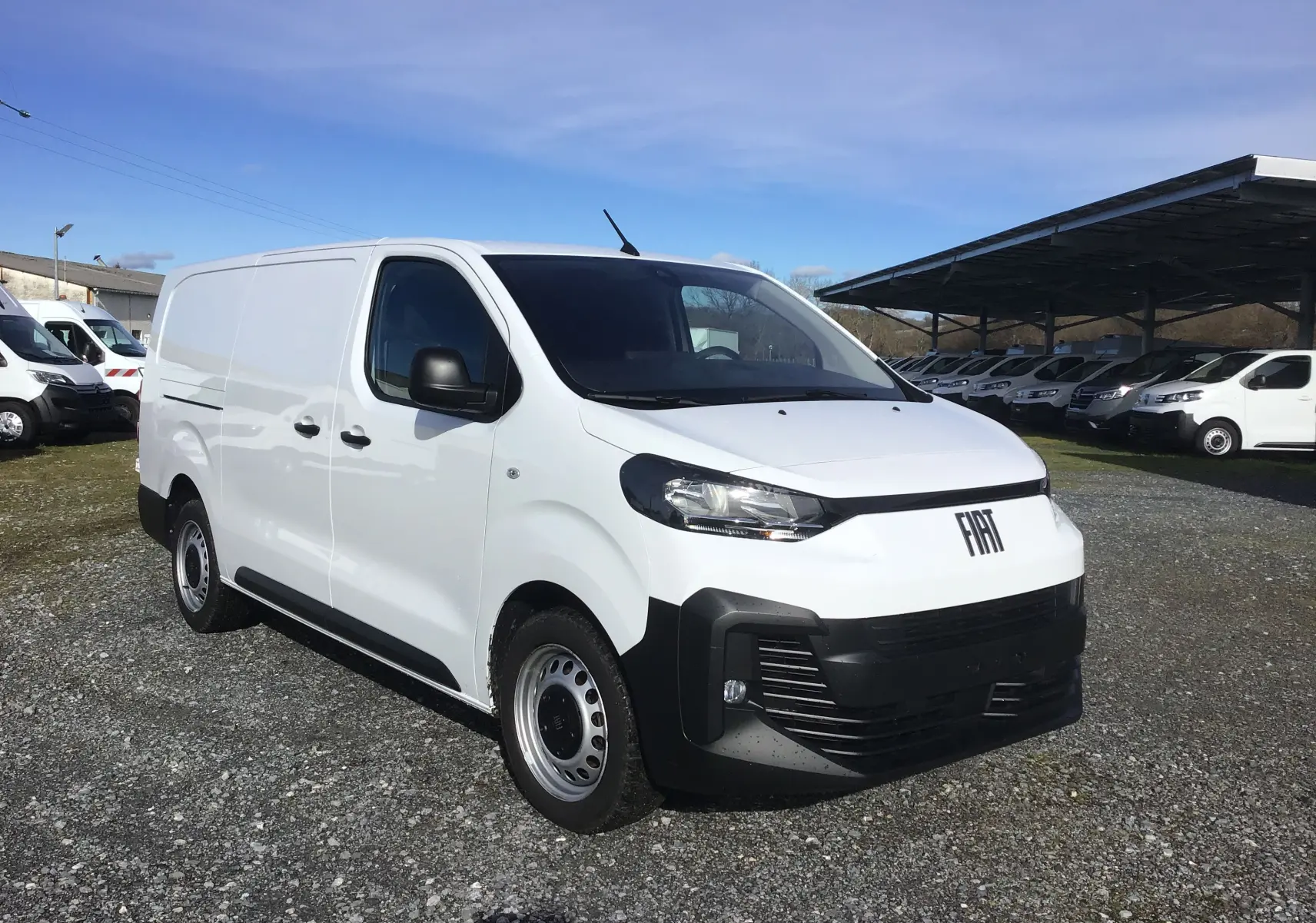 Vue 3/4 avant droite du FIAT Scudo Fourgon blanc 2024 avec pare-chocs noir et jantes acier, stationné sur un sol gravillonné.