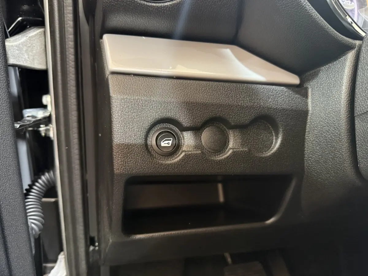 Gros plan sur le bouton d'ouverture du coffre côté conducteur dans l'habitacle de l'AIXAM AMBITION 0.5 CROSSOVER PREMIUM 2026.