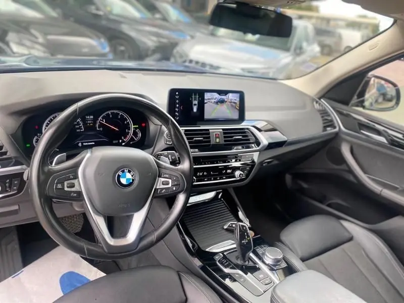 Vue intérieure côté conducteur du BMW X3 X-Drive 20 DA 2018 avec tableau de bord moderne et écran central affichant la caméra de recul.