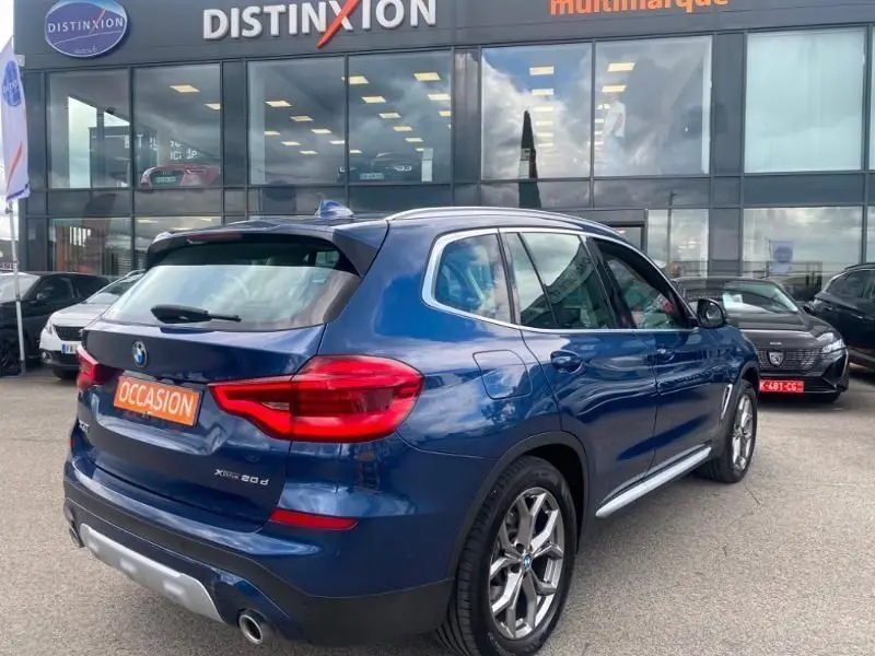 BMW X3 X-DRIVE 20 DA bleu métal, vue 3/4 arrière droit, avec badge X-Line et plaque "OCCASION" visible.
