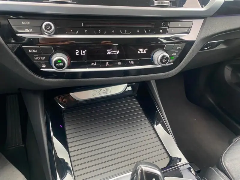 Vue rapprochée de la console centrale noire brillante du BMW X3 X-DRIVE 20 DA avec commandes climatisation et logo X3.