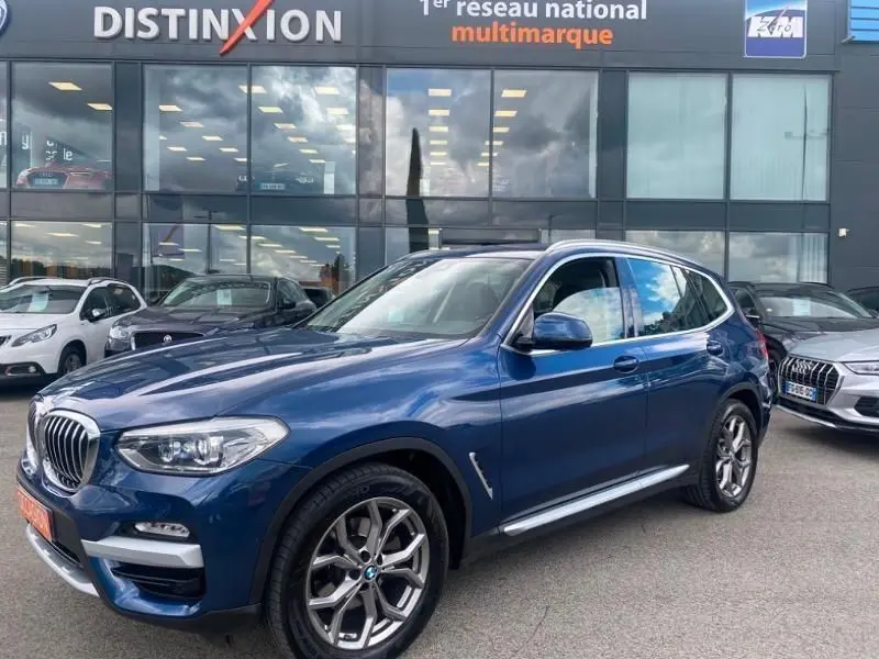 BMW X3 X-DRIVE 20 DA bleu métal vue 3/4 avant droit, avec jantes alliage et calandre caractéristique X-Line.