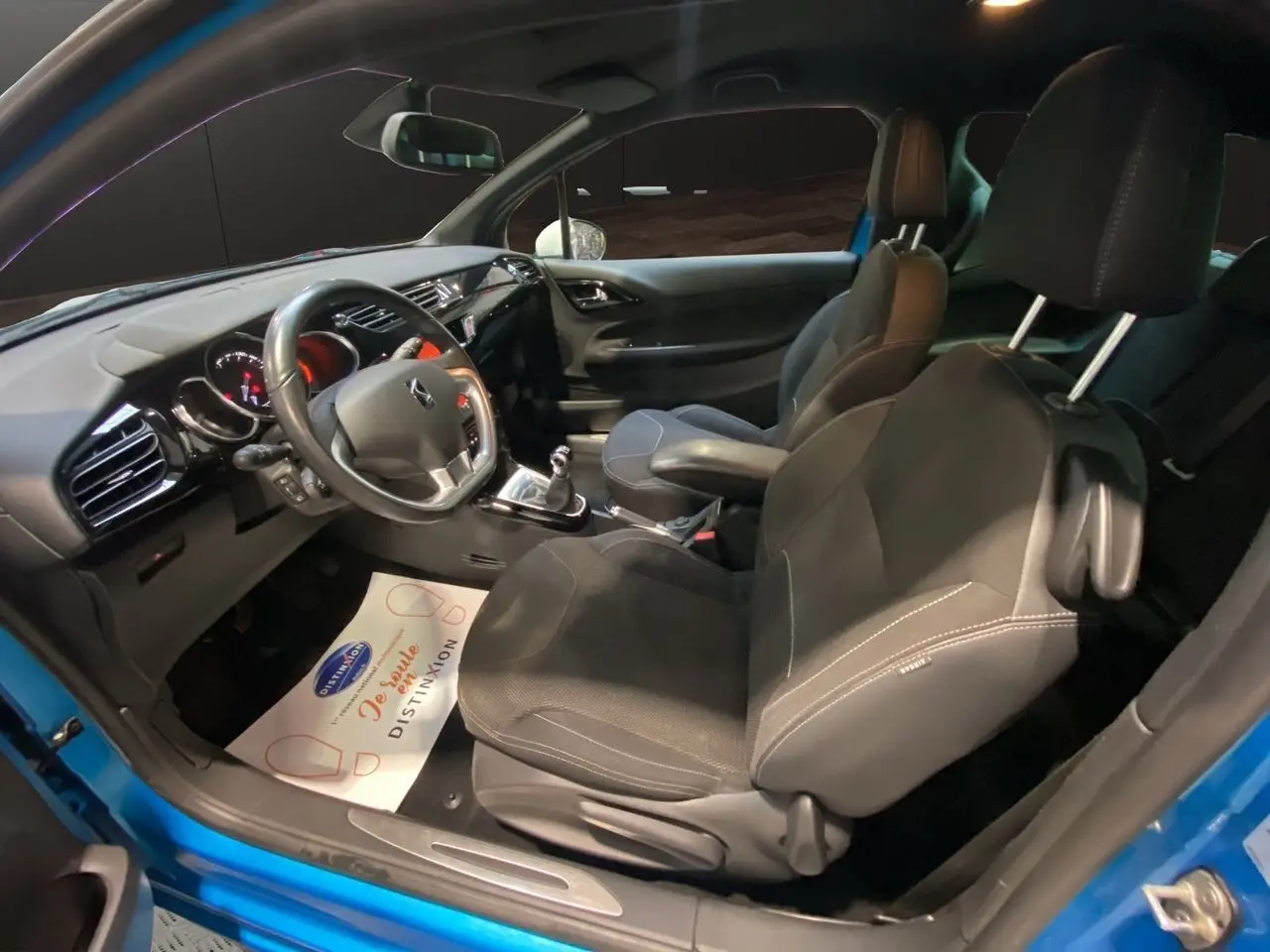 Vue intérieure côté conducteur d'une Citroën DS3 bleu avec toit blanc, sièges noirs et volant multifonction.