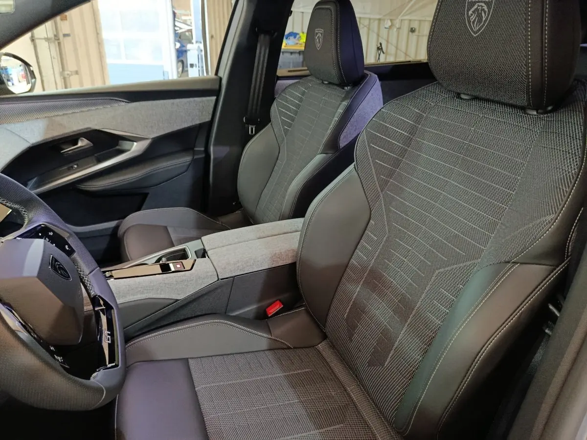 Vue intérieure côté conducteur du Peugeot 5008 GT 2026, sièges tissu et cuir gris avec logo lion brodé sur appuie-tête.