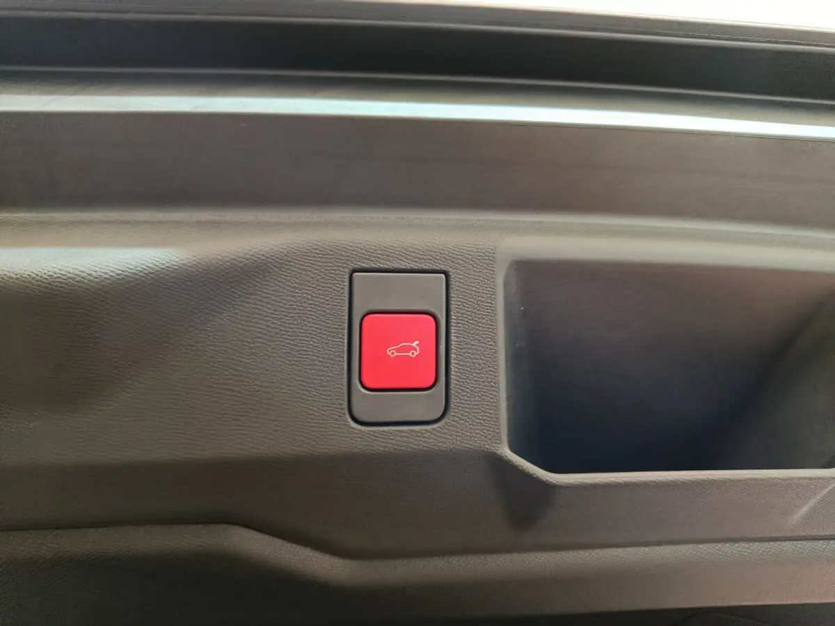 Bouton rouge d'ouverture électrique du coffre sur panneau intérieur noir du Peugeot 5008 gris clair, vue rapprochée.