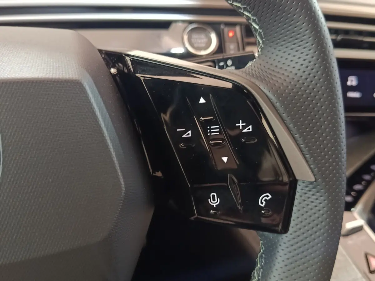 Gros plan sur les commandes noires du volant cuir perforé du Peugeot 5008 gris clair, version hybride rechargeable 2026.