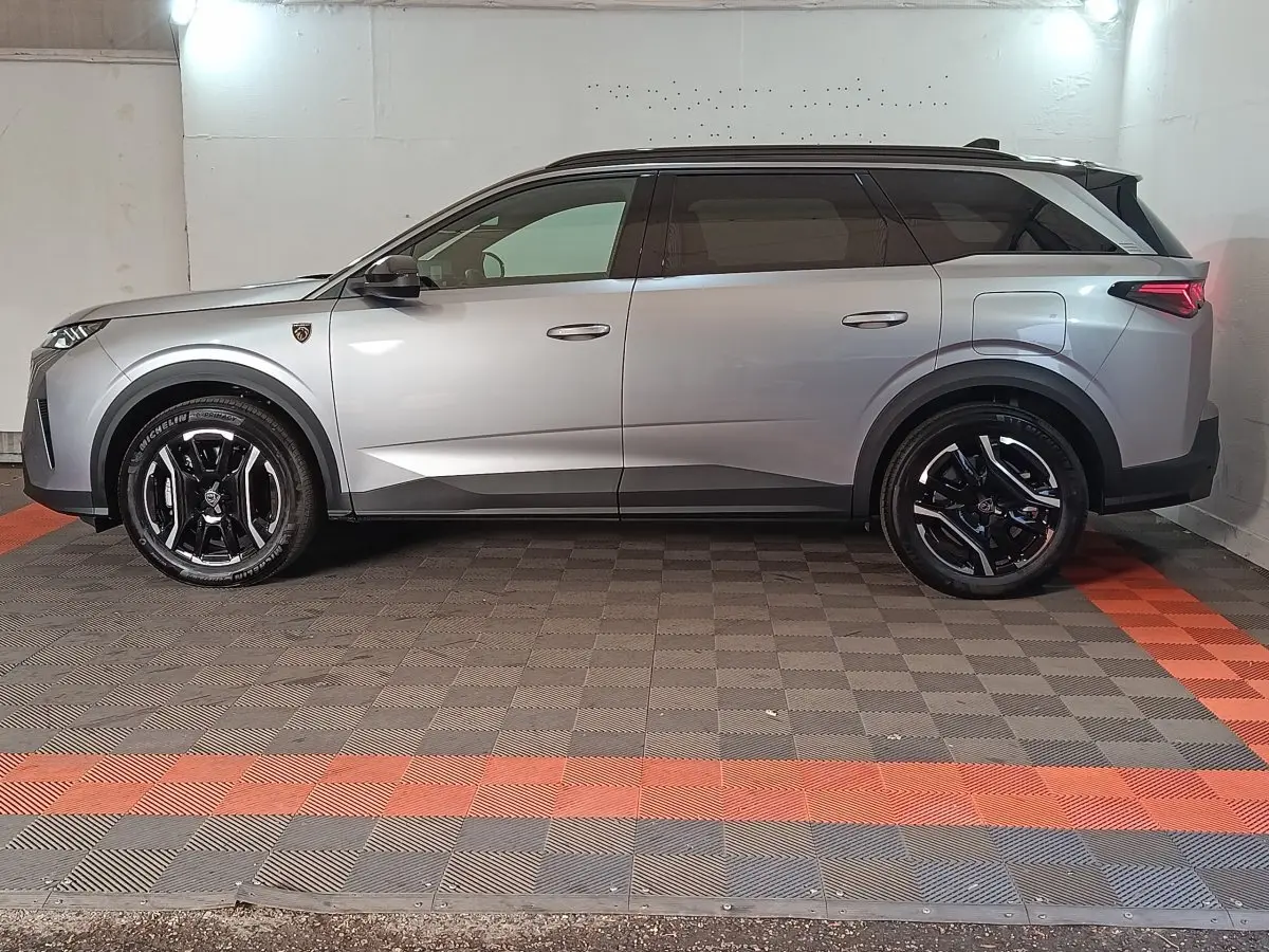 Vue de profil côté gauche d'un Peugeot 5008 gris clair avec jantes noires et toit noir dans un garage.