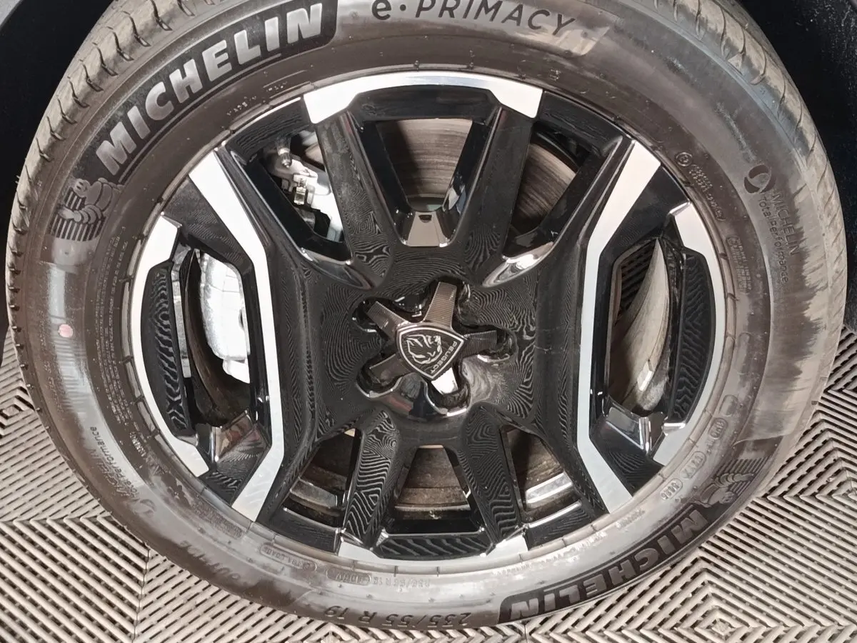 Gros plan sur la jante noire et argentée avec logo Peugeot, montée d’un pneu Michelin sur Peugeot 5008 gris clair.