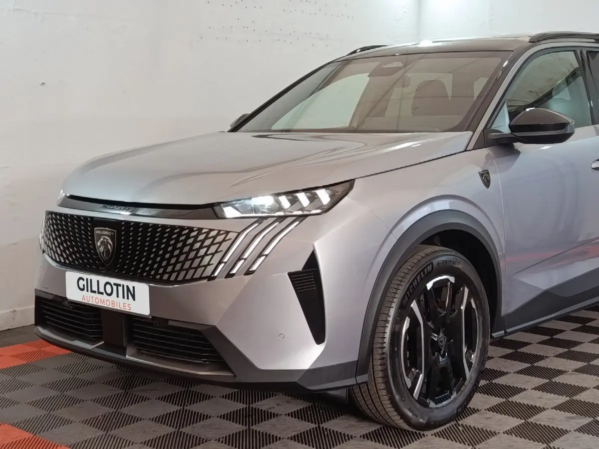 Vue 3/4 avant droit du Peugeot 5008 gris clair avec calandre noire et phares LED allumés.