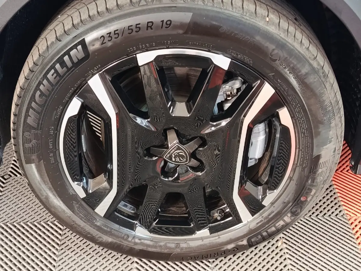 Gros plan sur la roue avant droite du Peugeot 5008 gris clair, avec jante noire et argentée au design moderne.