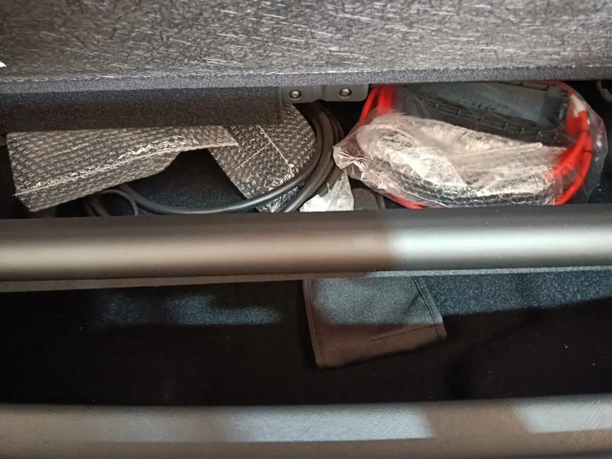 Coffre ouvert du Peugeot 5008 gris clair, montrant câbles et accessoires de recharge rangés sous la tablette.