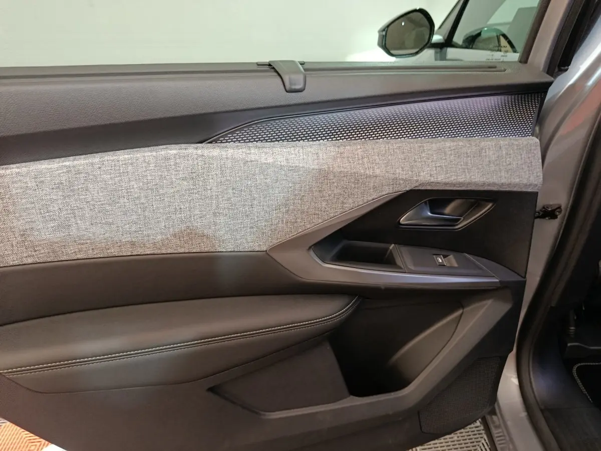 Gros plan sur la porte intérieure côté droit du Peugeot 5008 gris clair, avec habillage tissu gris et commandes de fenêtre.