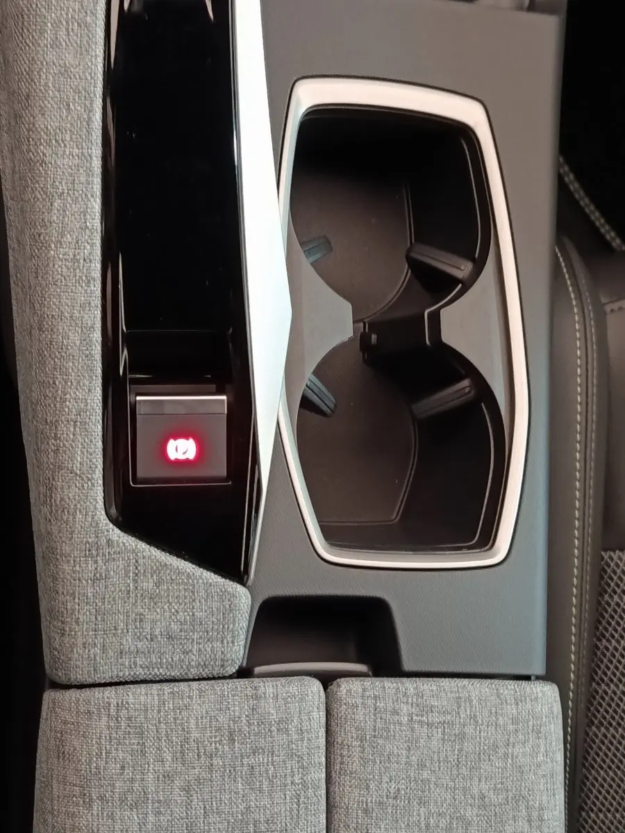 Gros plan sur la console centrale grise du Peugeot 5008 2026 avec porte-gobelets et bouton frein électrique rouge allumé.