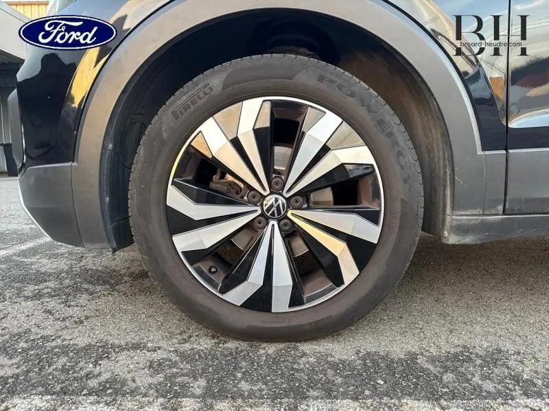 Gros plan sur la roue avant gauche d'un Volkswagen T-Cross noir nacré avec jante alu bicolore distinctive.