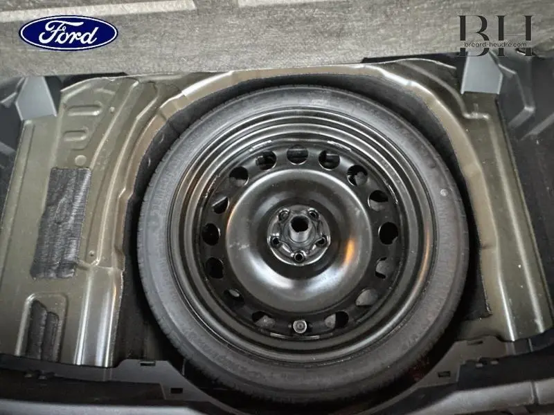 Gros plan sur la roue de secours noire en acier du coffre d'un Volkswagen T-Cross Noir Intense nacrée.