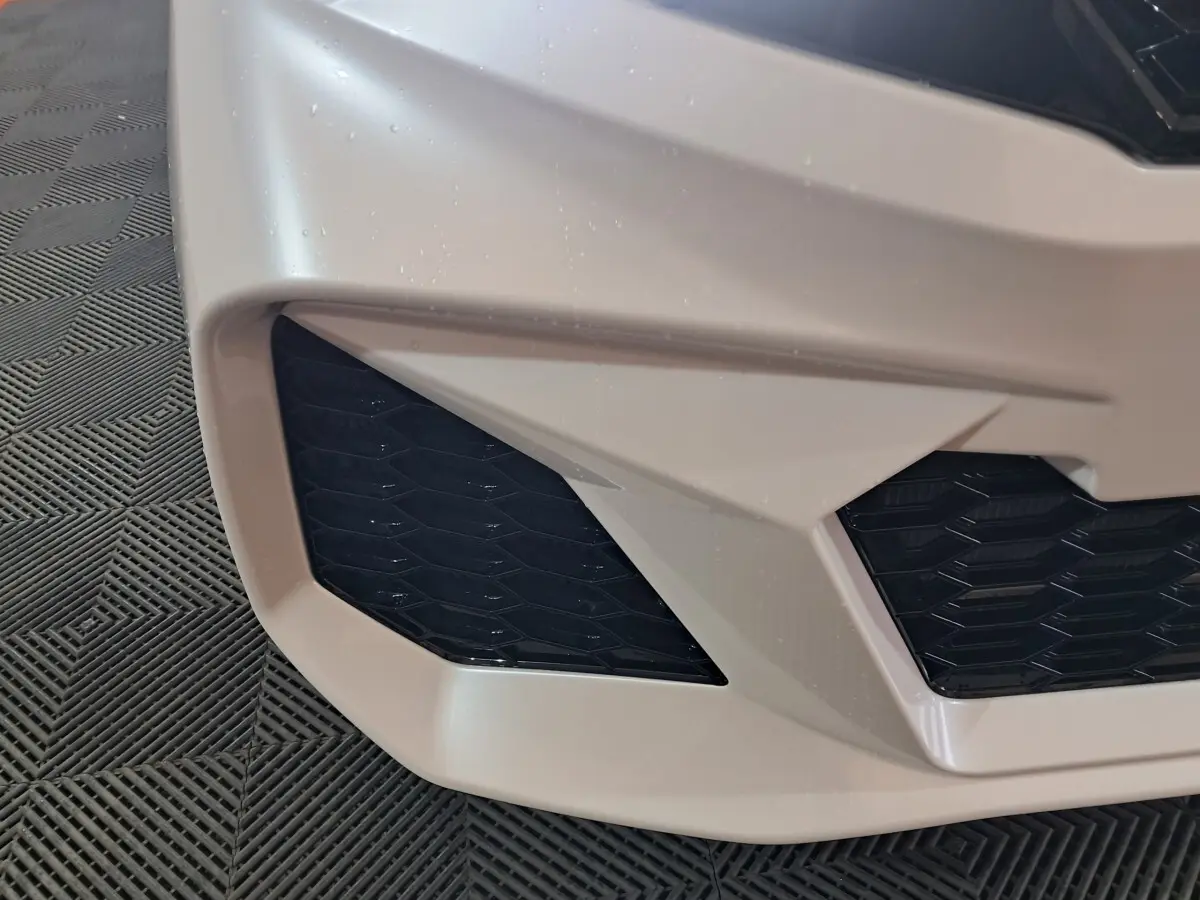 Gros plan sur la partie avant gauche blanche de l'AIXAM AMBITION 0.5 CITY COUPE GTI avec grille noire texturée.