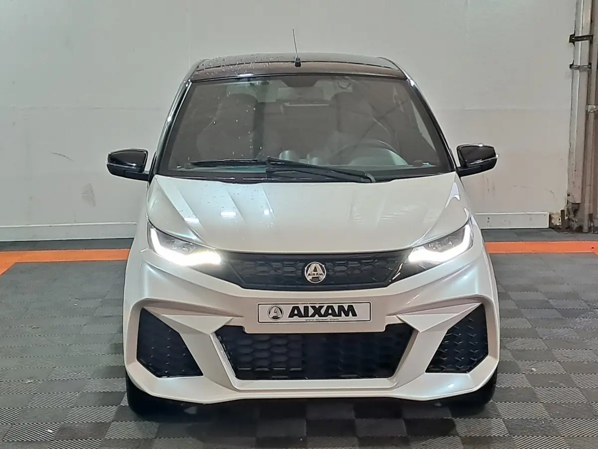 Vue de face d'une Aixam Ambition 0.5 City Coupe GTI blanche avec phares allumés et rétroviseurs noirs.