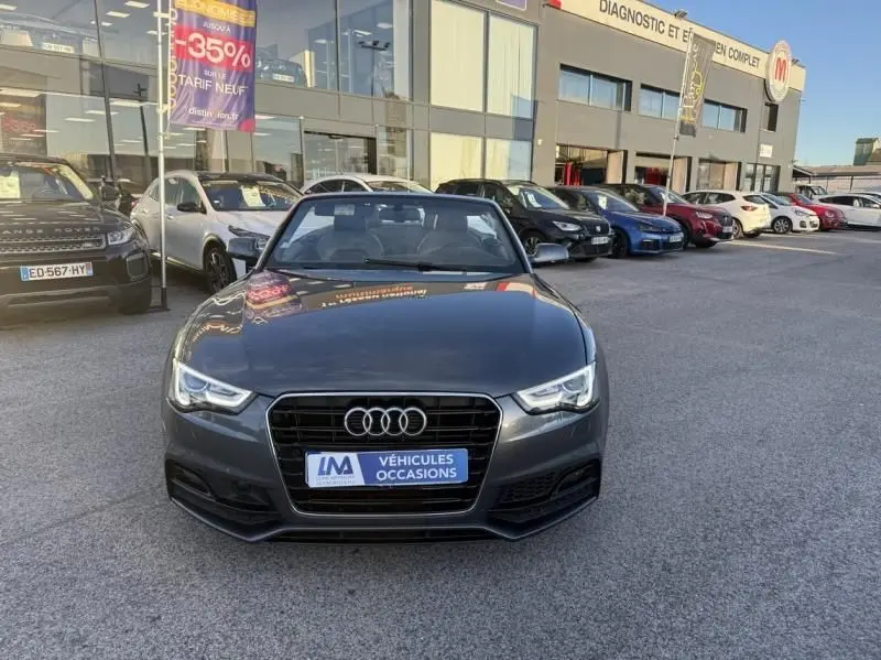 Vue avant d'une Audi A5 Cabriolet gris métal 2016 avec calandre S-Line et toit ouvert, stationnée en extérieur.