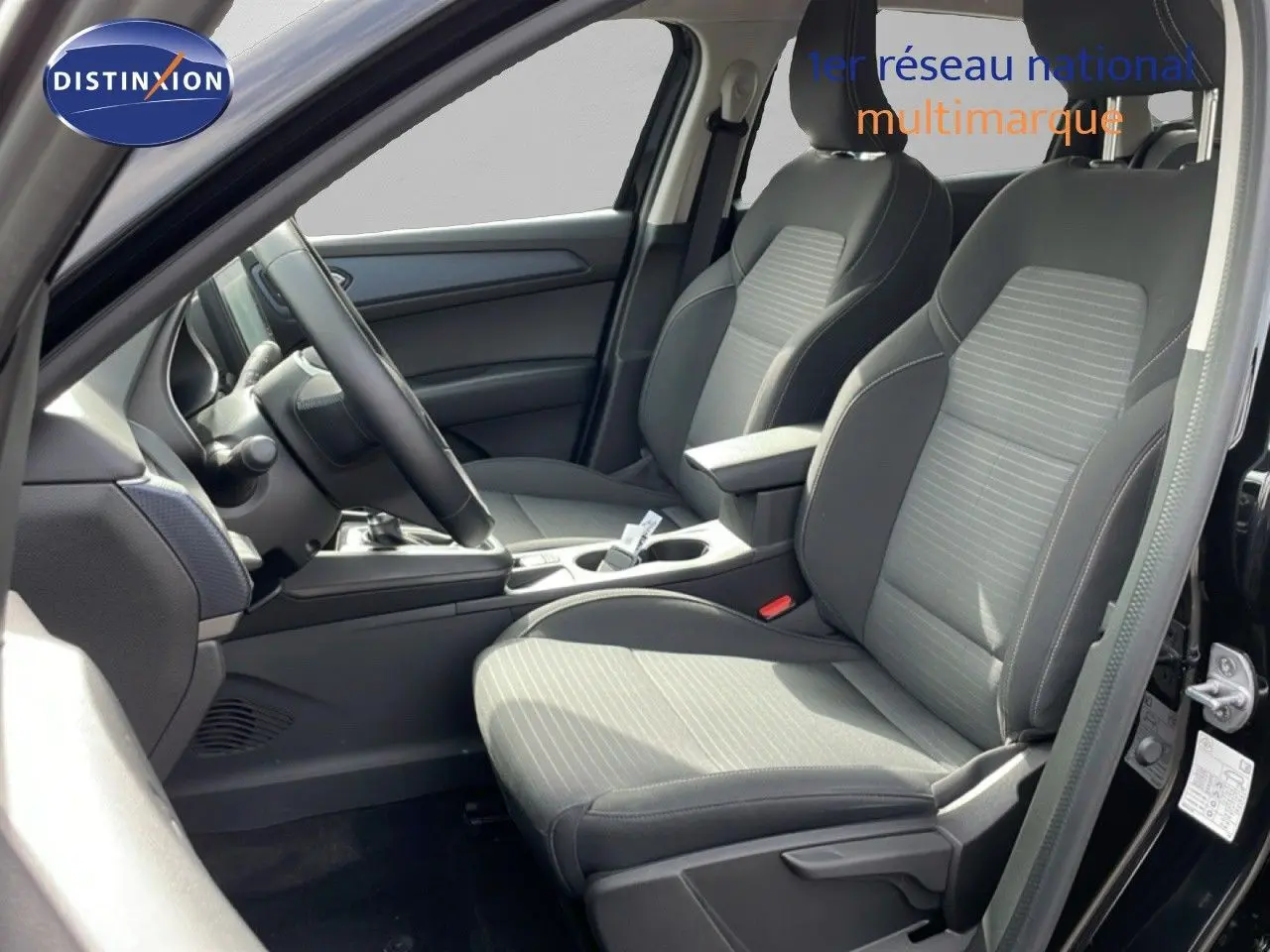 Vue intérieure côté conducteur de la Renault Arkana 2024 noir métal, sièges tissu gris avec console centrale et volant multifonction.