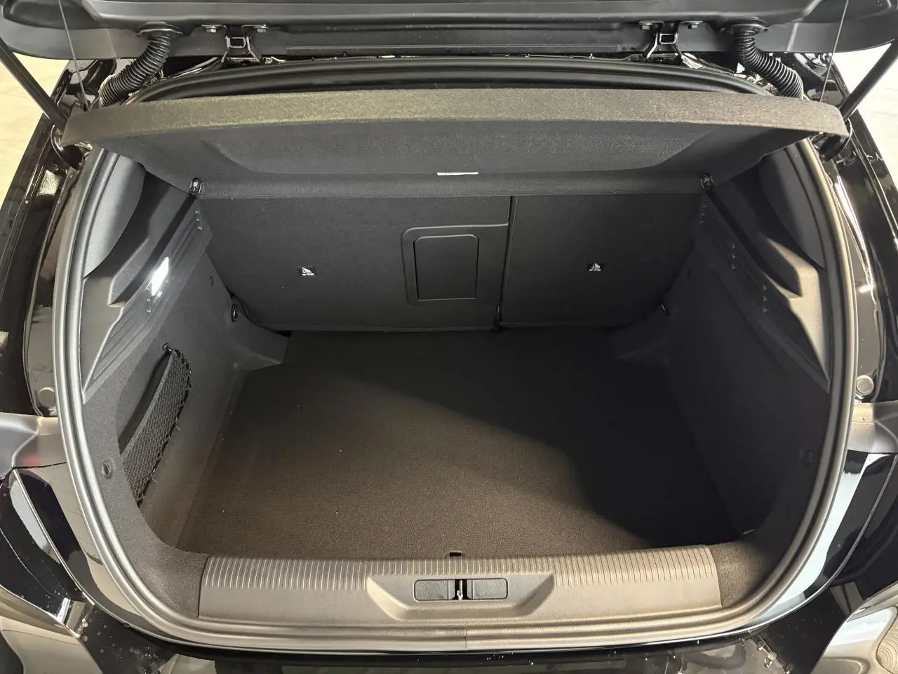 Coffre ouvert vu de dessus d'une Peugeot 308 noire métallisée, montrant l'espace de rangement et la moquette noire.