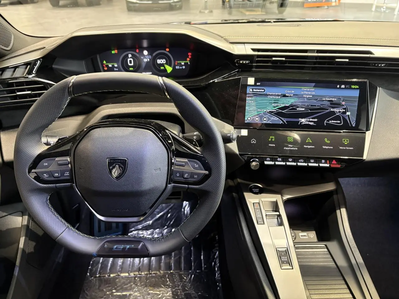 Vue intérieure centrée sur le volant GT cuir noir avec surpiqûres vert Adamite et écran tactile de navigation Peugeot 308 2026.